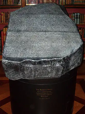 "Replica of the Rosetta Stone in the King's Library of the British Museum as it would have appeared to 19th century visitors, open to the air, held in a cradle that is at a slight angle from the horizontal and available to touch"
