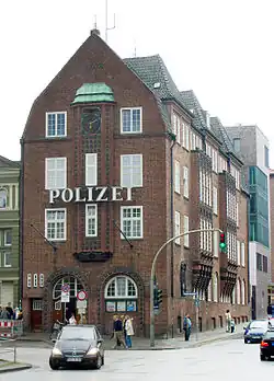 A 3 floor red-brick building, with the German word 'police' in large letters between first and second floor. The windows are white sash windows.