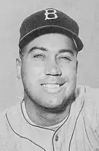 A black and white headshot of an older baseball player, looking ahead and smiling, wearing a baseball cap with a 'B' on it.