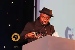 Man accepting award, wearing black hat and top.