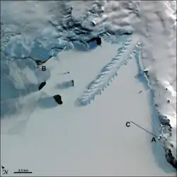 aerial view of a frozen bay, with a long peninsula of ice protruding from a snow-covered shoreline