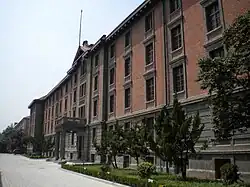A red brick building with regular windows and a stone-faced ground floor. It is seen looking along its front; in the center there is a small entrance pavilion with a pediment at the roofline above it
