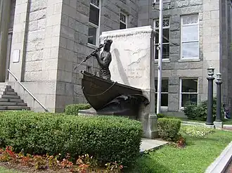 Statue of a whaler holding a harpoon. Text reads "a dead whale or a stove boat" engraved on stone behind the statue.