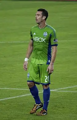 A man wearing a green soccer uniform standing on a field.